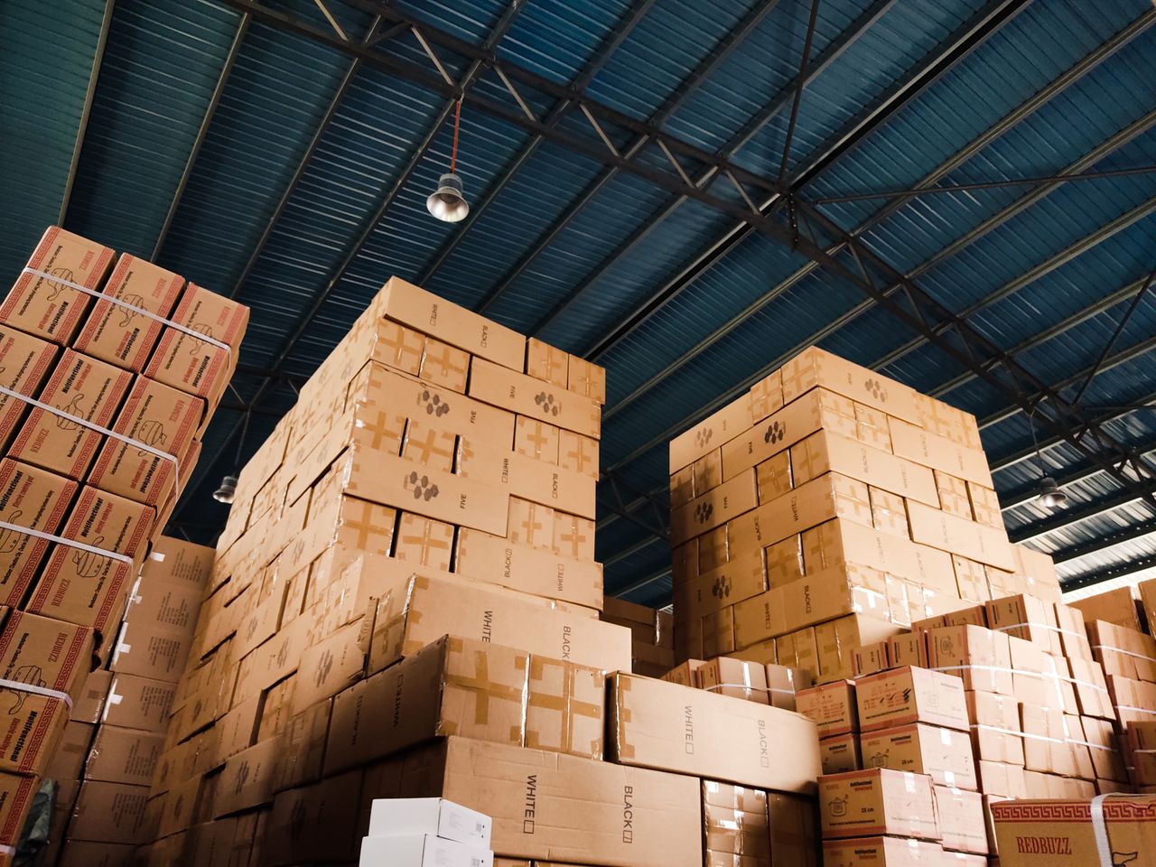 Mastering the First Impression: Your intriguing post title goes here High stacks of cardboard boxes organized in a warehouse with a blue metal ceiling.