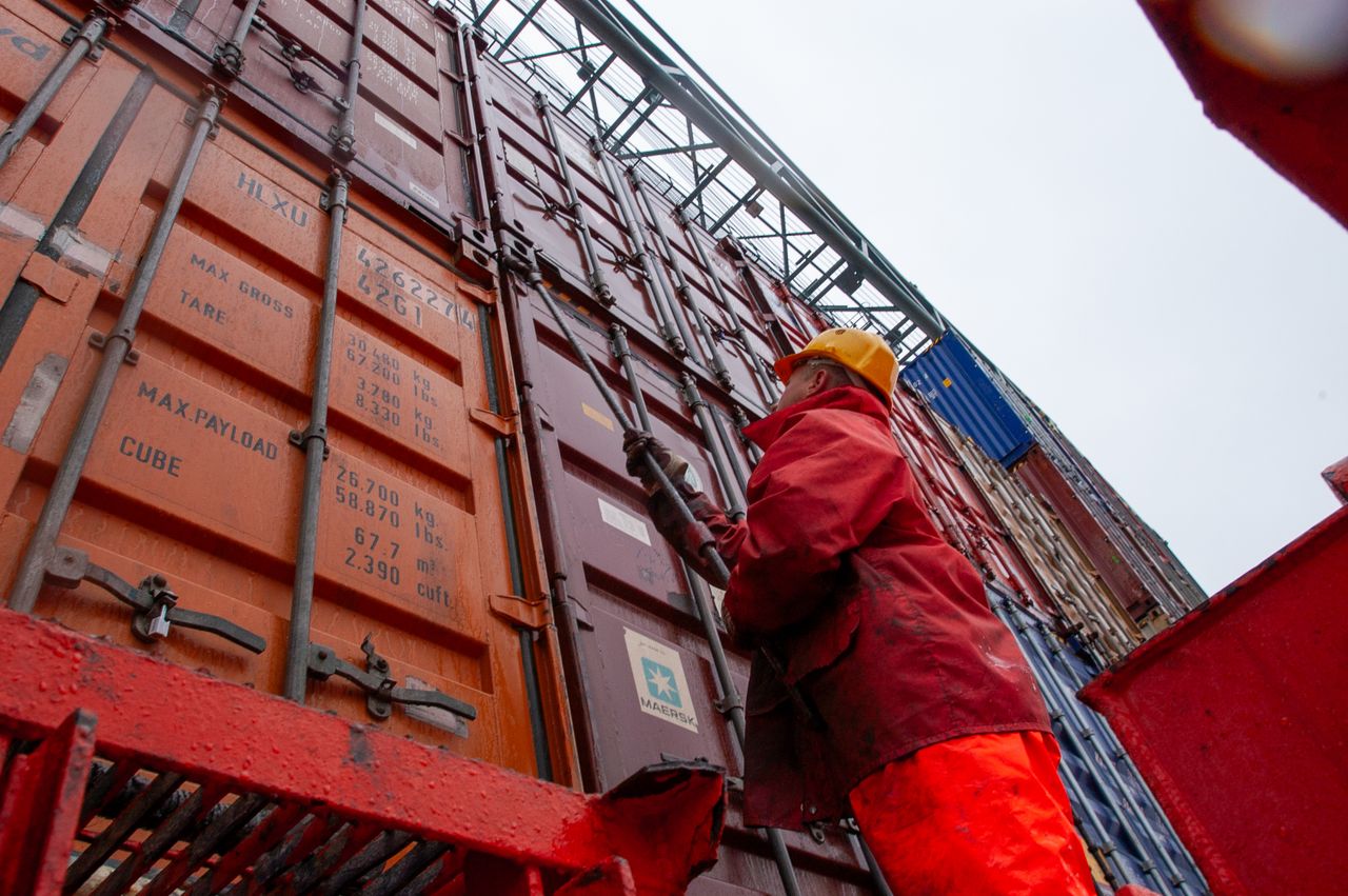About Industrial worker securing cargo containers on a rainy day at a shipping port.