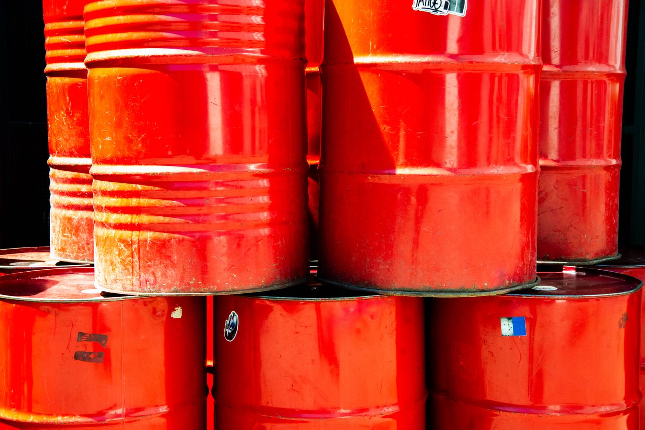 Services Bright red industrial oil barrels stacked outdoors in daylight, showcasing vivid color and industrial theme.